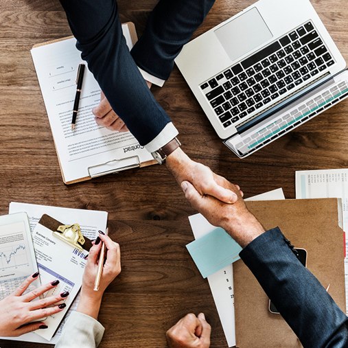 Poignee de main au-dessus de documents et ordinateur pour illustrer le consulting SEO